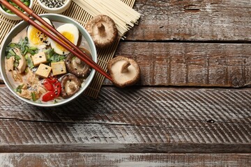 Noodle soup. Bowl of delicious ramen and chopsticks on wooden table, flat lay. Space for text