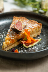Sliced of pie decorated with fresh figs on a black ceramic plate.