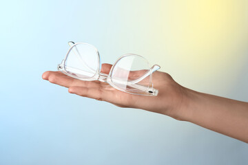 Woman holding glasses with transparent frame on color background, closeup