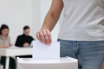 Woman putting her vote into ballot box on blurred background, closeup