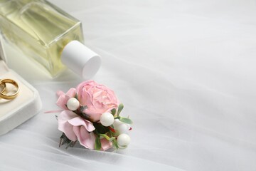 Obraz na płótnie Canvas Wedding stuff. Stylish boutonniere, wedding rings and perfume bottle on white veil, closeup pace for text