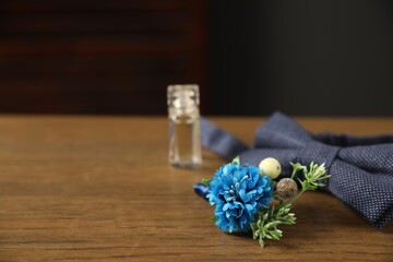 Wedding stuff. Stylish boutonniere, bow tie and perfume bottle on wooden table, closeup. Space for text
