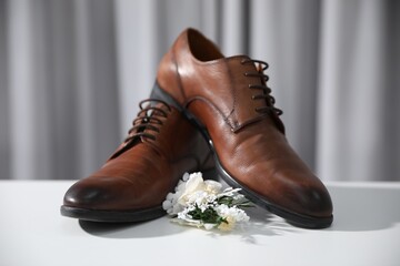 Wedding stuff. Stylish boutonniere and brown shoes on white surface against gray background, closeup - obrazy, fototapety, plakaty