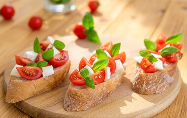 Fototapeta na wymiar Caprese bruschetta with tomatoes, mozzarella cheese and basil in sun rays on wooden board. Traditional Italian appetizer, snack or antipasto. Vegetarian food. Healthy eating. Mediterranean food.