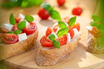 Bruschetta with cherry tomatoes, mozzarella cheese and basil in sun rays on wooden board. Traditional Italian appetizer, snack or antipasto. Vegetarian food. Healthy eating. Mediterranean food.