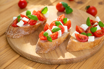 Bruschetta with cherry tomatoes, mozzarella cheese and basil in sun rays on wooden board. Traditional Italian appetizer, snack or antipasto. Vegetarian food. Healthy eating. Mediterranean food.