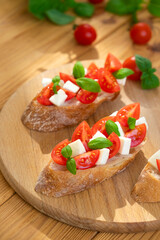Caprese bruschetta with tomatoes, mozzarella cheese and basil in sun rays on wooden board. Traditional Italian appetizer, snack or antipasto. Vegetarian food. Healthy eating. Mediterranean food.