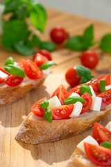 Fototapeta na wymiar Caprese bruschetta with tomatoes, mozzarella cheese and basil in sun rays on wooden board. Traditional Italian appetizer, snack or antipasto. Vegetarian food. Healthy eating. Mediterranean food.