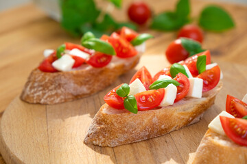 Caprese bruschetta with tomatoes, mozzarella cheese and basil in sun rays on wooden board. Traditional Italian appetizer, snack or antipasto. Vegetarian food. Healthy eating. Mediterranean food.