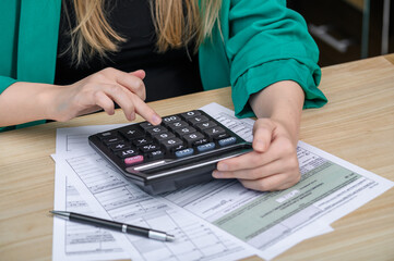 Kobieta pracująca w biurze księgowym liczy na kalkulatorze i wypełnia deklaracje podatkowe