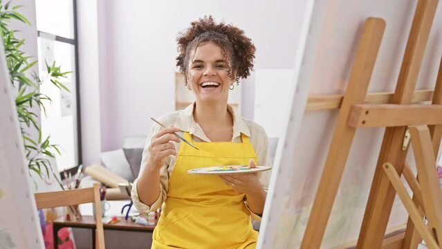 Cool, confident, and happy hispanic artist, woman with perfect smile and curly hair sitting joyfully in the studio