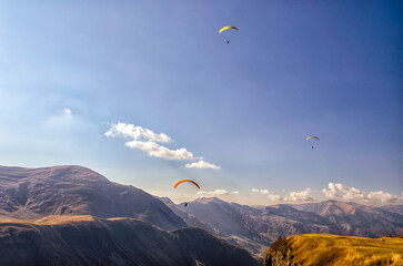 three paragliders in sky against the background of Caucasus mountains