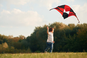 Little boy is playing outdoors at daytime. Standing, having fun with kite
