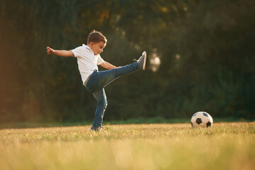Fototapeta na wymiar Side view, playing soccer. Little boy is playing outdoors at daytime