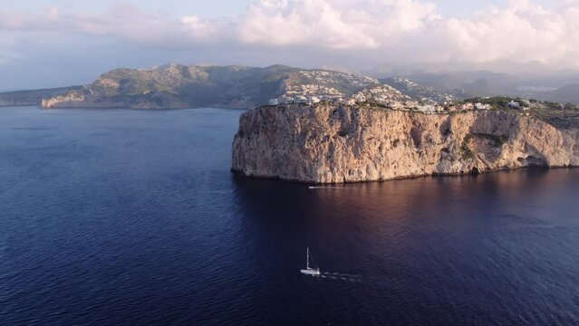 Aerial drone shot of private boat charter navigate close to Mallorca island during summer daylight. Breathtaking view of epic cliff with Mallorca sea view property on the top. Exclusive yacht rental. 