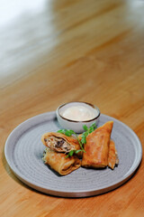 Filled pancakes, decorated with sprigs of dill, cut in half on a plate, served with sour cream.