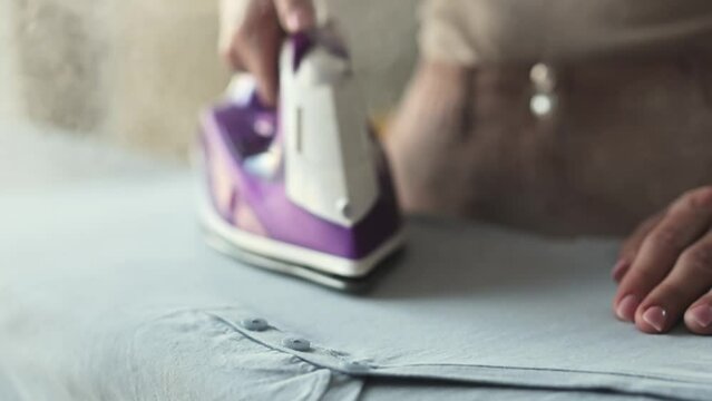 Girl hand using iron with steam mode for wrinkled clothes, closeup view. Woman with hot electric tool smoothing textile