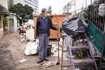 Man, working and cleaning of garbage for waste management in city with portrait, broom and happiness. Person, face and smile by dumpster site for scrap, recycling and trash in neighborhood for litter