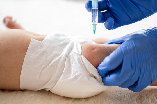 Close up view of syringe needle injecting vaccine into baby leg.