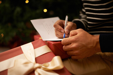 Writing, hands and man with card and gift for Christmas event or party at home for family....