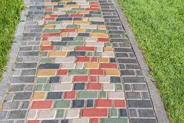 Colorful paved road across lush lawn on sunny day. Pathway with bright step stones in summer park. Creative design element of landscaping