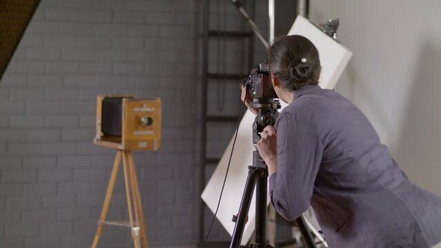Girl photographer. A photographer in a professional photo studio takes pictures of a retro camera on a wooden tripod. Photographer's work. Take photographs on film in a medium format camera. 