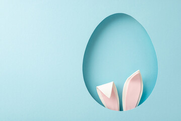 Playful Easter inspiration photo. Top view of humorous bunny ears peeking from an ovoid gap on a...