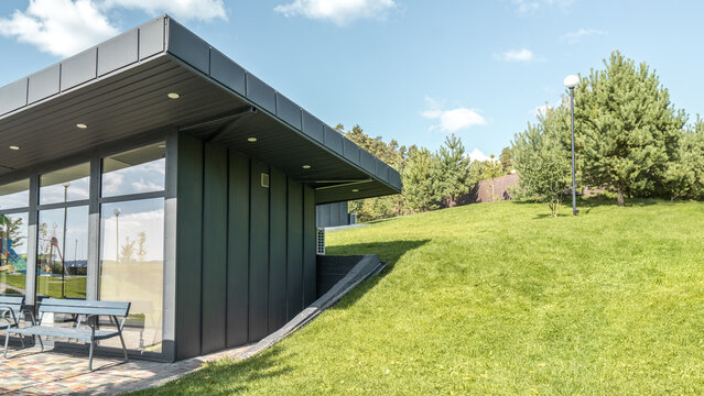 Modern guest house with standing seam facade panoramic glazing and large flat roof overhang in park. Minimalist architectural style of public building