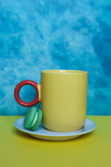 Yellow cup of coffee with colorful macaroon on yellow and blue background