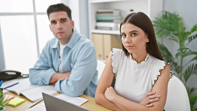 A focused woman and a thoughtful man sit in a modern office, embodying professionalism and teamwork.