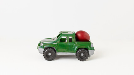 A green toy car carries an Easter egg on a white background