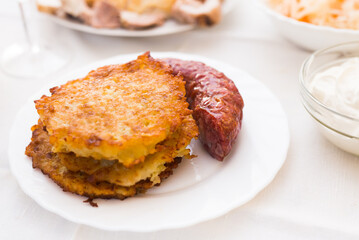 Fried grated potato pancakes with fried sausage on white plate