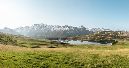 Klare Morgenstimmung mit spiegelglattem See und schneebedecken Bergen im Hintergrund und saftiger...