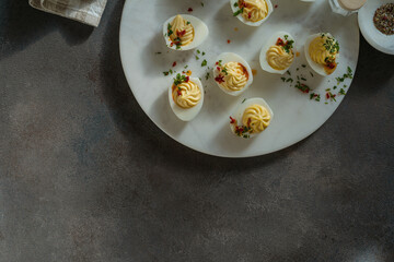 Deviled eggs with spicy oil on dark gray background with sunligh and harsh shadows, directly above