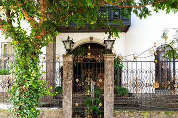 Entrance of pretty white house, with black ironwork gate and security fence with gold details, San...