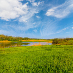 Obraz premium small lake among green hills at calm bright spring day, seasonal countryside landscape