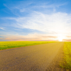 long asphalt road among green fields  leaving far at the sunset