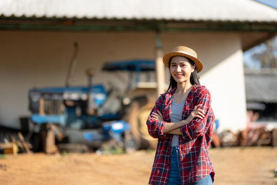 Proud female farmer stands with her arms crossed outdoors with a tractor behind her.