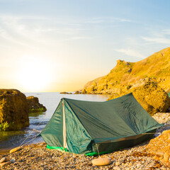 small touristic tent on a sea coast at the sunrise, early morning sea camping scene