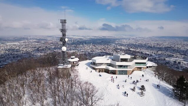 Sapporo, Japan: Aerial drone footage of the observatory at the top of snow covered Mt Moiwa overlooking Sapporo city downtown in winter in Hokkaido in northern Japan. Shot with an orbit motion. 