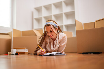 Modern ginger woman with braids writing in notebook while moving in new home. - 752308178