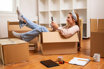 Happy woman using phone and having fun while moving into new apartment.