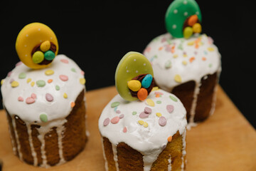 Easter cakes with white icing and colorful decorations on a wooden board on black background. 