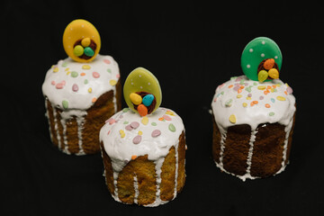 Easter cakes with white icing and colorful decorations for children on black background. 