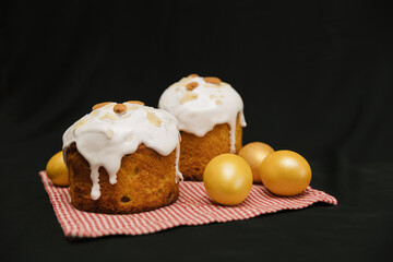 Easter cakes with white icing and almond nuts on serviette on black background. Yellow or gold eggs. Copy space. 