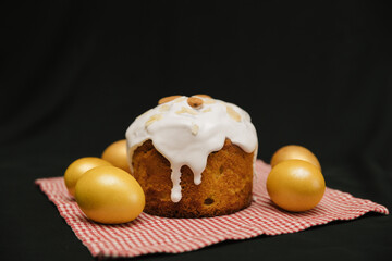Easter cake with white icing and almond nuts on serviette on black background. Yellow or gold eggs. Copy space. 