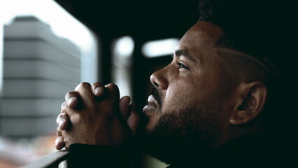 One faithful young hispanic black man in PRAYER gazing at SKY from balcony in deep mental contemplation. Profile close-up face of a SPIRITUAL South American 20s person