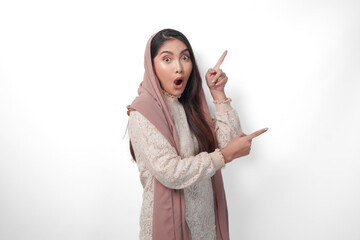 Surprised Asian Muslim woman wearing headscarf veil hijab looking shock while pointing to copy...