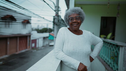 One happy elderly black woman from South America standing at humble residence balcony overlooking...