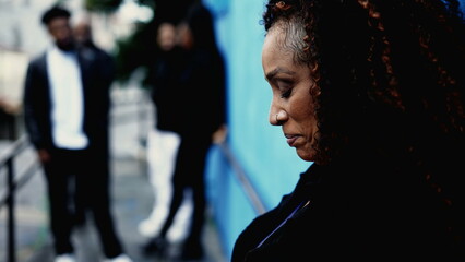 One pensive worried middle-aged black latina hispanic woman in deep contemplative dilemma standing in urban street leaning on blue wall struggling with depression